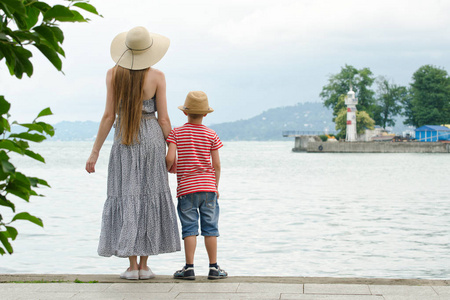 妈妈和儿子站在码头上的海面背景 灯塔和远处的群山。后视图