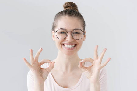 美丽女孩戴大圆眼镜的灰色背景分离寻找快乐和积极的因为她显示双 ok 的手势，在将来被确定最佳结果的室内照片