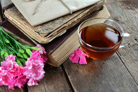 旧书与美丽的花朵和杯茶木制的桌子上关闭