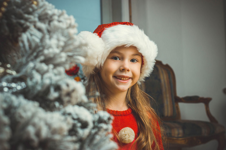 可爱的快乐女孩，在附近的圣诞树顶红色的帽子