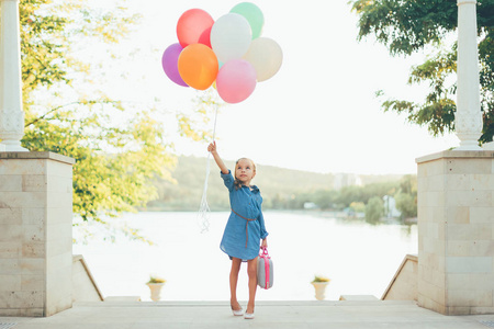 性格开朗的女孩，抱着五颜六色的气球带着孩子气的手提箱