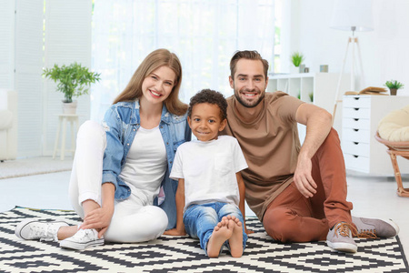 幸福的夫妇与收养的非洲裔美国男孩坐在地毯在家