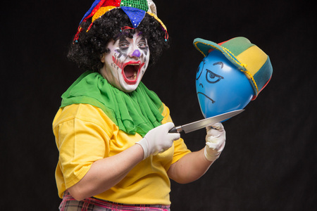 生气的丑陋小丑想要杀死一个戴着帽子的气球