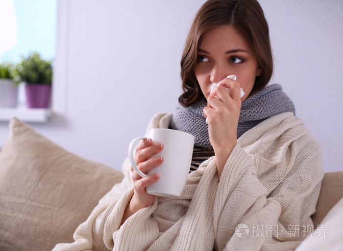 一个生病的女人坐在沙发上吹她的鼻子的肖像