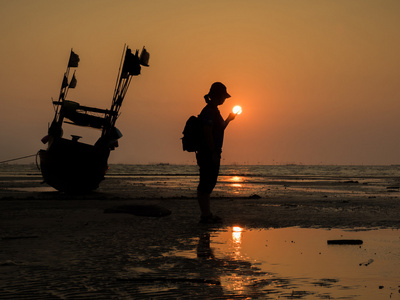 一个女孩和渔船在日落海滩上的剪影