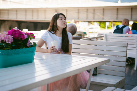 夏季咖啡馆户外可爱亚洲的年轻女人。在白色的 t 恤，简单光温馨的装修风格的餐厅，市区的长发的女孩