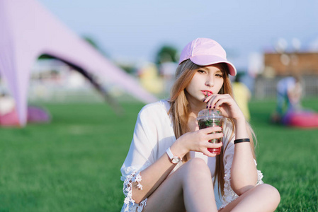 年轻漂亮的女孩时髦饮料提神柠檬水红在公园里休息。夏天的概念。看着摄像机