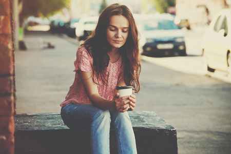 漂亮的女孩坐在街与早晨喝咖啡