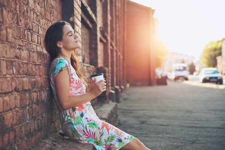 漂亮的女孩坐在街与早晨喝咖啡和放松