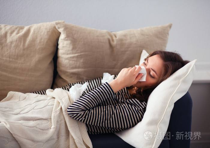 一个生病的女人坐在沙发上吹她的鼻子的肖像