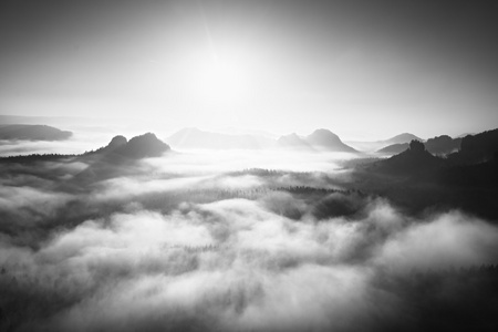 与视图到迷雾笼罩的山谷岩石山顶的神奇日出。黑色和白色