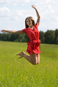 年轻女孩穿着红色的在外地的针叶林中跳跃