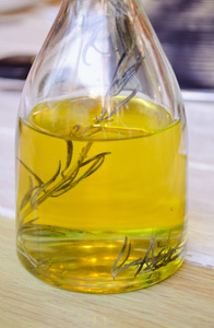 瓶橄榄油和迷迭香里面一枝。在一个木制的表面透明玻璃瓶