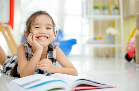 可爱的亚洲女孩读一本书，微笑牙齿白时住的房间里