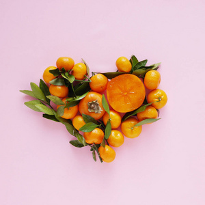 粉红色的背景下的小橘子, 叶子和柿子制成的心