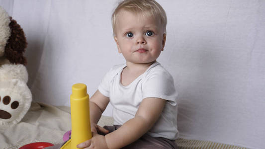 一个漂亮的小男孩的肖像, 坐在玩玩具金字塔, 金发, 浅色, 蓝色的眼睛, 白色背景。概念 婴儿, 美丽的皮肤, 漂亮的孩子
