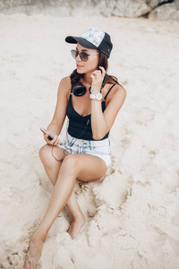 妇女使用智能手机听音乐与耳机在海滩