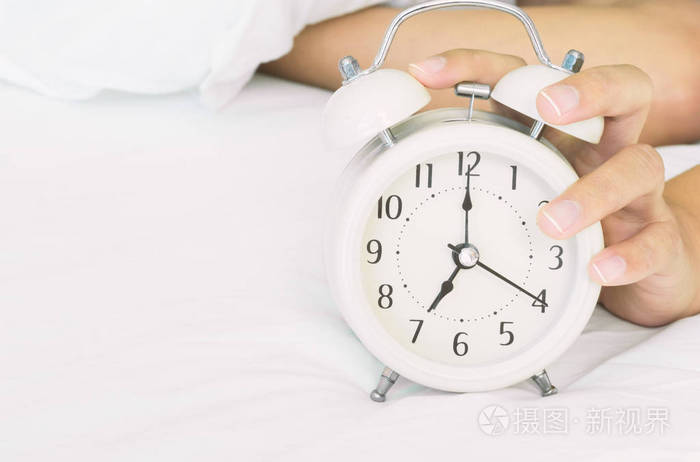 特写女人手在清晨白床上关掉闹钟 唤醒时间概念