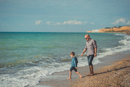 爸爸和儿子沿着海滨漫步。爸爸和儿子沿着海边走。周末在海滩。沙滩石海沫
