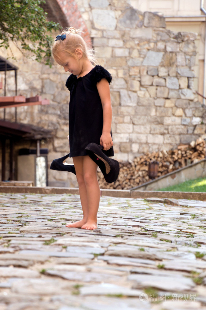 小女孩抱着她的鞋和看台赤脚的道路上