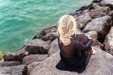 浪漫的金发女人，穿着黑色连衣裙在湖边休息