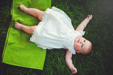 一个半岁的孩子躺在院子里的草地上, 穿着一件白色的连衣裙, 6 月。儿童儿童用品的概念教育