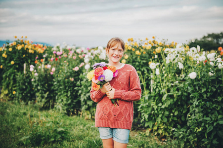 户外肖像可爱的小女孩手持彩色花束的大丽花花, 穿着时尚套衫
