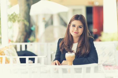 亚洲年轻的商界女坐在咖啡馆中与冰咖啡