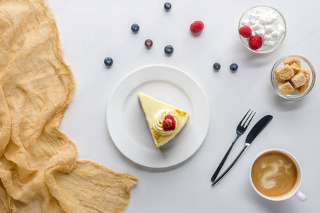 白色桌面上的浆果和咖啡的一块蛋糕的顶部视图