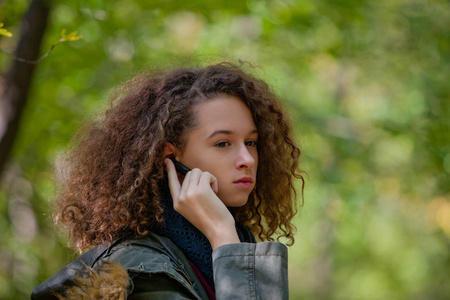 卷曲的头发十几岁的女孩在秋季森林智能手机