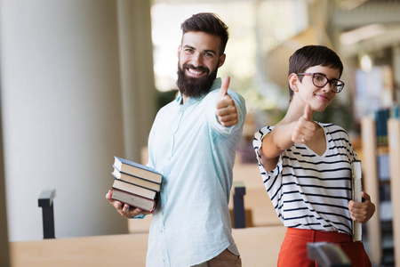 学生们在图书馆学习。年轻英俊的男人和有吸引力的女人一起学习, 并显示竖起大拇指