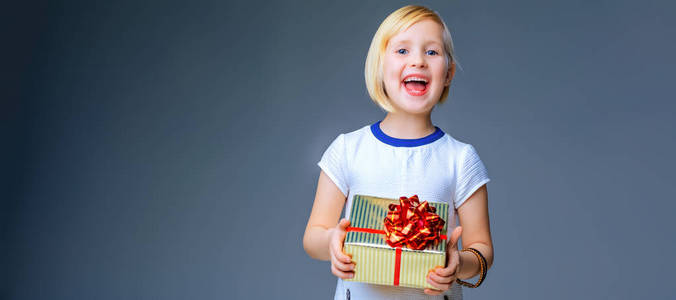 现代的女孩。快乐的时尚女孩，在灰色的背景，与圣诞礼物盒上孤立的白色连衣裙