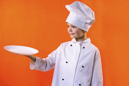滑稽的男孩厨师厨师拿着盘子为面团在橙色背景