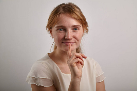 年轻女子与生姜头发穿着休闲奶油白色上衣触摸嘴唇, 而沉默的标志