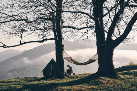 秋天野营在山, 垂悬的吊床在树, 人坐在背景