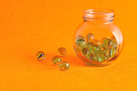 收集了一些在橘黄色的背景上显示的玻璃罐子里的弹珠