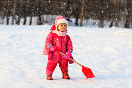 可爱的小姑娘蹒跚学步挖在冬天的雪