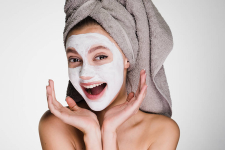 女人用一条毛巾在她的头上应用一个白色的面具来清洁脸上的皮肤