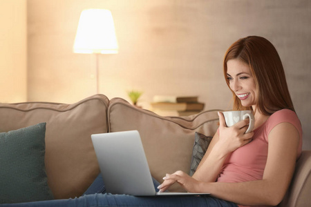在家用手提电脑的美丽的微笑的妇女用杯子茶