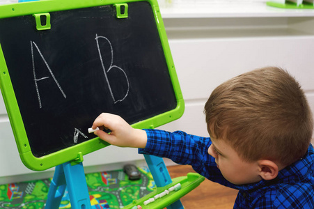 一个小男孩用粉笔在黑板上画字母。儿童教育概念