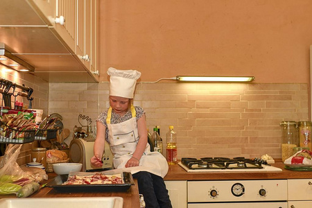 小女孩在厨房里的一个厨师服装。可爱的小女孩准备比萨饼