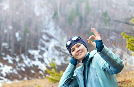 好的雪坡和森林背景上的年轻女子旅游 pokazyet 标志