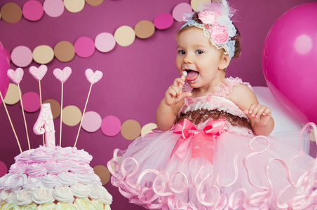 一个小快乐的生日女孩的肖像与第一个蛋糕。吃第一块蛋糕粉碎蛋糕