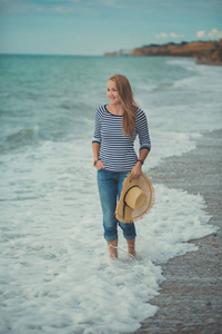 可爱的美女夏娃在沙滩上独自漫步海滩海边度假穿着时髦蓝色牛仔裤衬衫和巨大的帽子与敏感的沙崖海角景观
