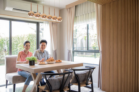 年轻亚裔夫妇吃油炸鸡肉一起在客厅里的当代民居的现代生活方式的概念