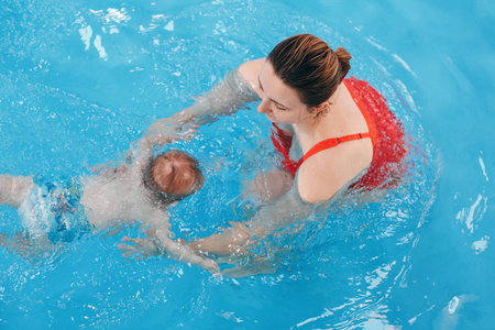 白种白人母亲训练她的新生婴儿在游泳池里漂浮。婴儿在水中潜水。健康积极的生活方式。家庭活动与早期发展观