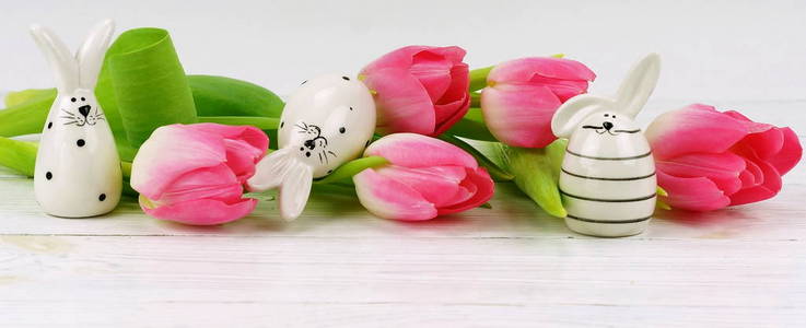 复活节兔子和一束粉红色的郁金香在白色的木制背景。复制空间. 横幅