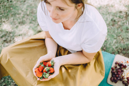 年轻的黑发妇女在野餐吃新鲜的草莓
