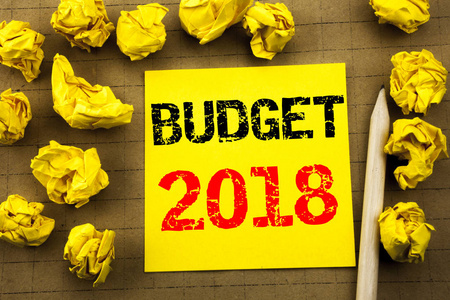 显示预算2018的手写文本。家庭预算核算计划的商业概念写在黄色复古背景上的粘纸条纸上。背景上的折叠黄色纸张