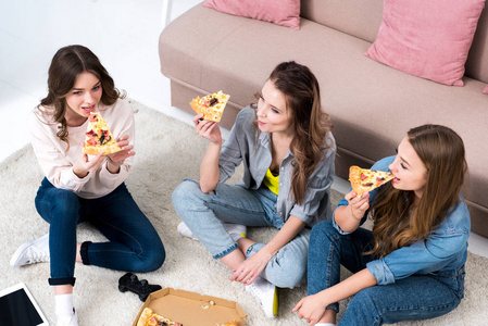 高角度看美丽的微笑的年轻妇女吃比萨饼和在家聊天
